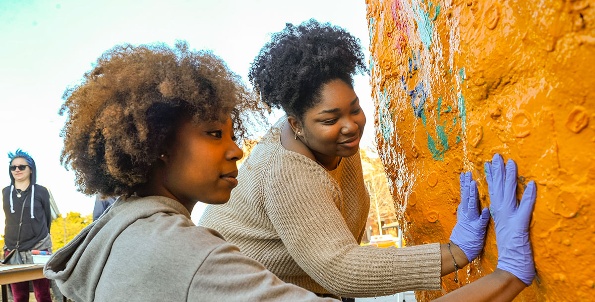 Two students painting a rock on campus.